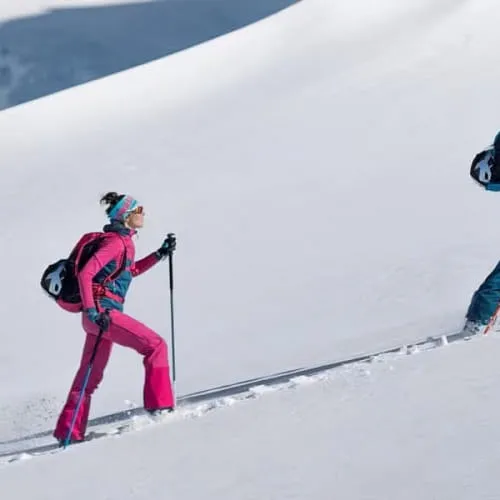 Three skiers ascend a snowy slope wearing colorful gear