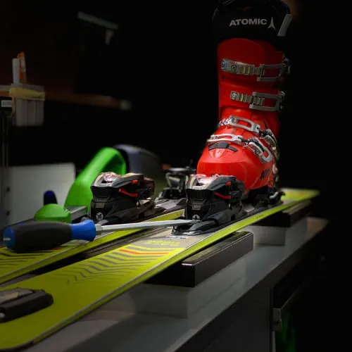 Skisportuitrusting met rode schoen en bindingen op een groene ski